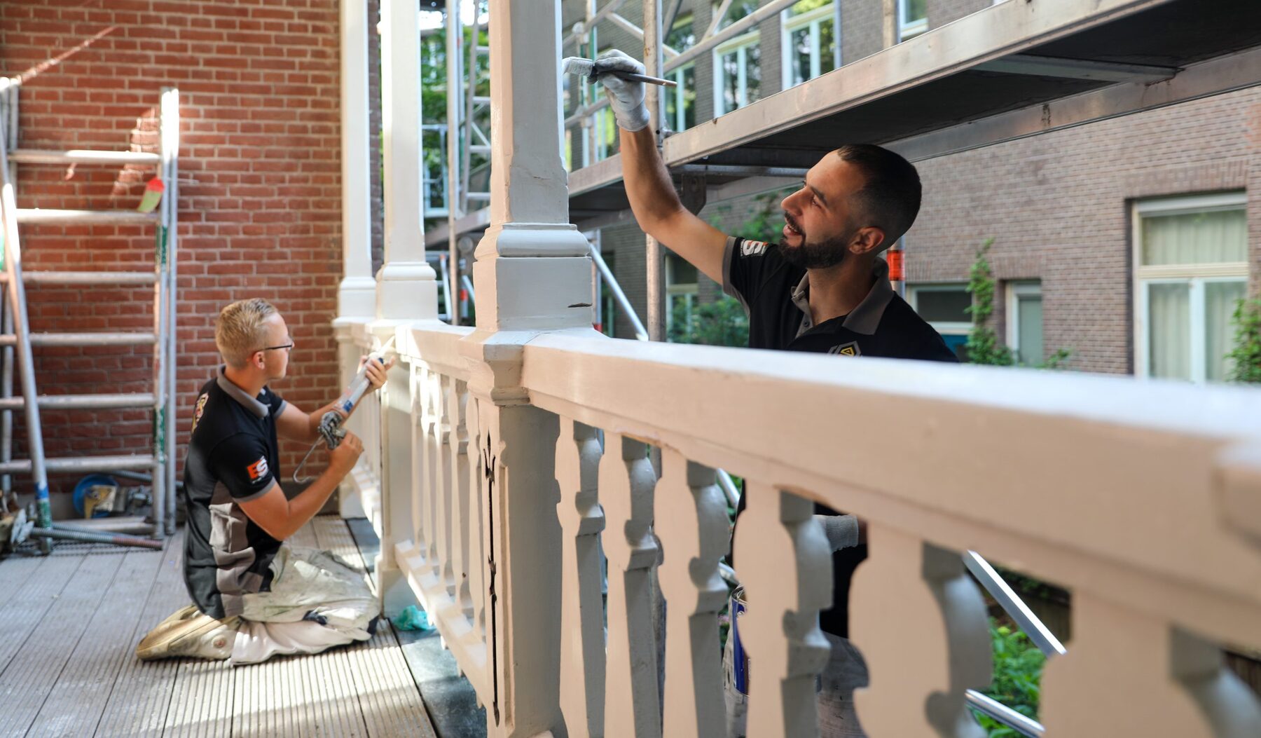 Twee schilders werken aan een balustrade op een dakterras